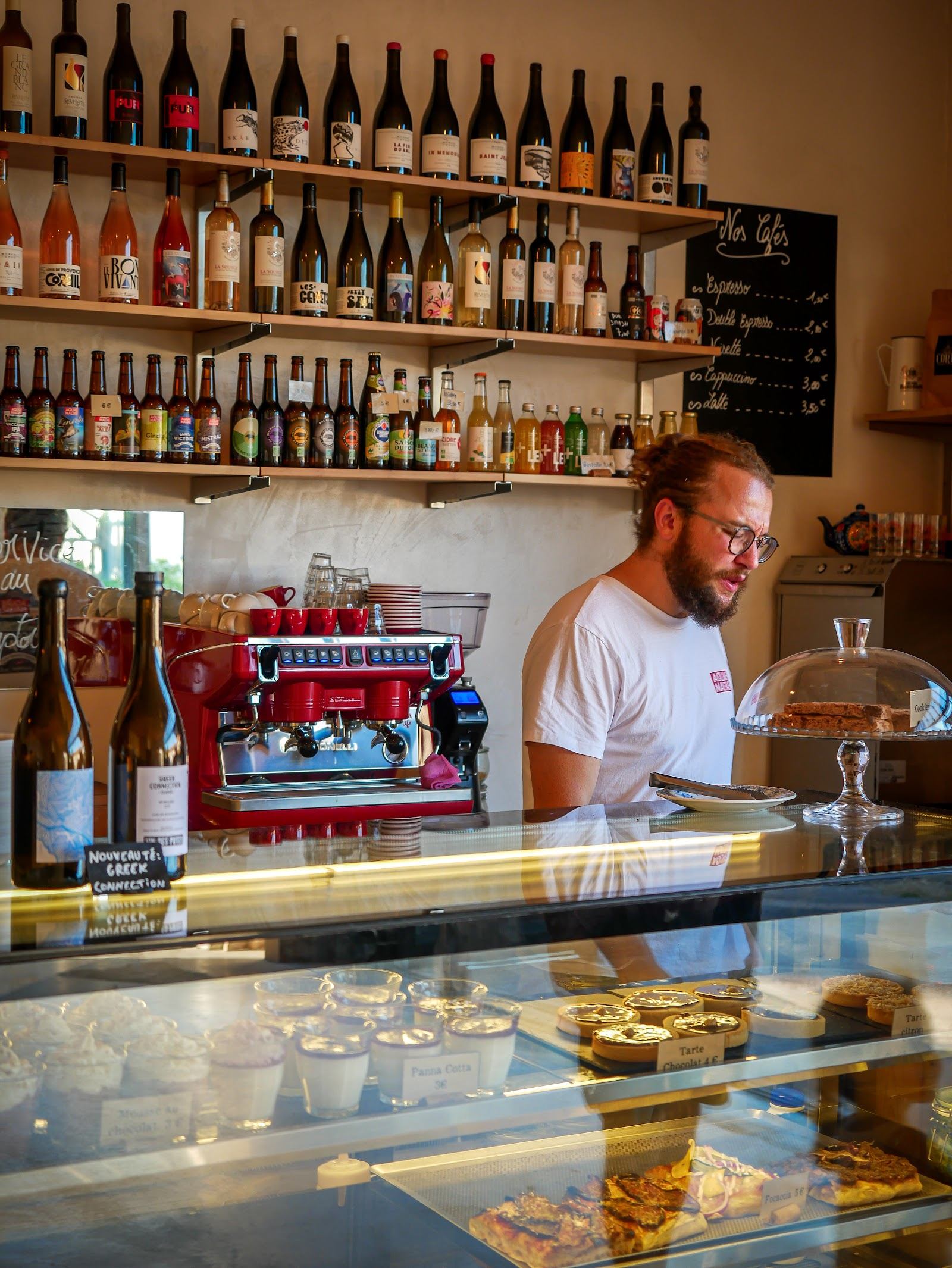 Le comptoir de Lo Pichotòme : machine à café rouge, étagères de bouteilles et vitrine de pâtisseries