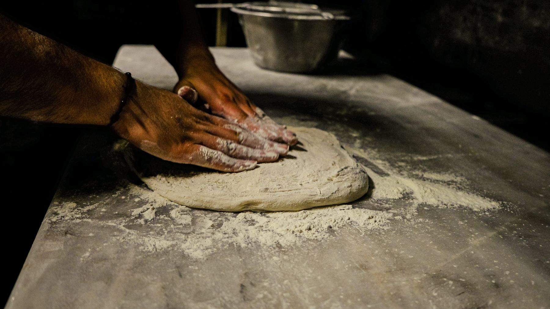 Des mains pétrissent une pâte à pizza dans la farine